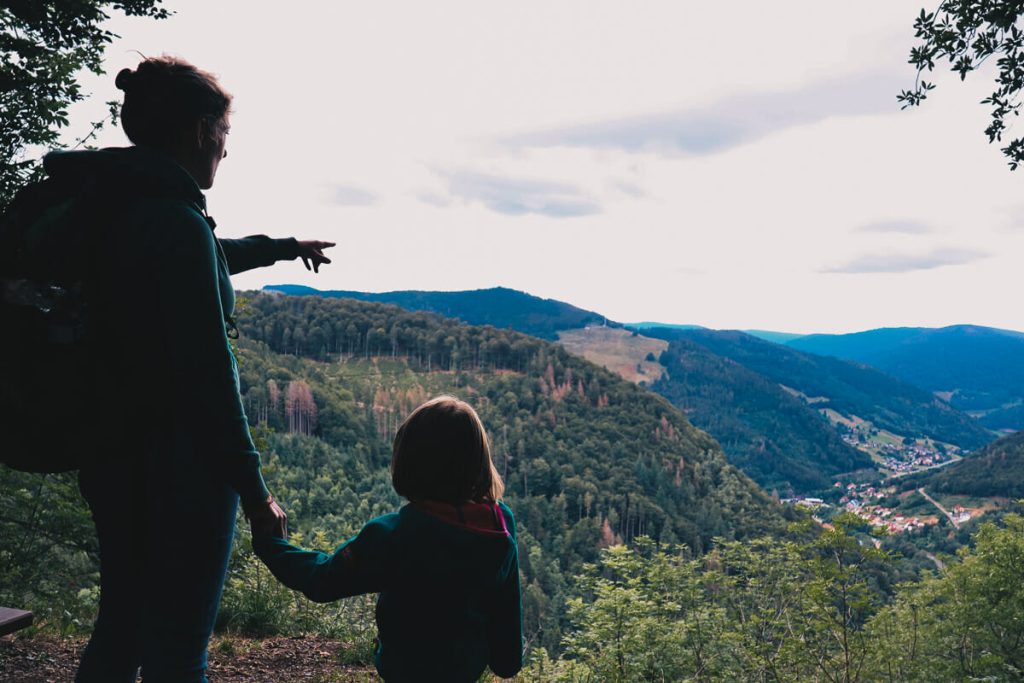 Mère et fille en silhouette au sommet d'un point de vue en Forêt Noire admirant le panorama sur les montagnes et un village allemand