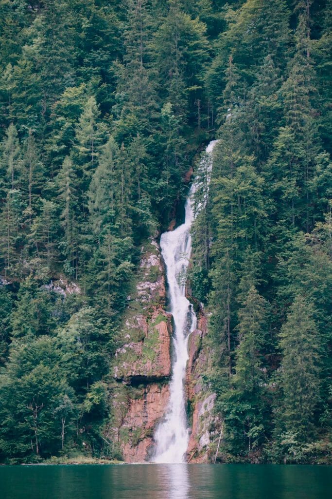 Vue plongeante sur la cascade de Röthbachfall se déversant depuis les falaises boisées dans les eaux émeraude du lac Königssee en Bavière