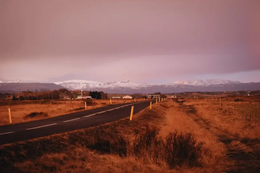 Route goudronnée dans le Cercle d'Or s'étendant vers les montagnes enneigées sous une lumière dorée.