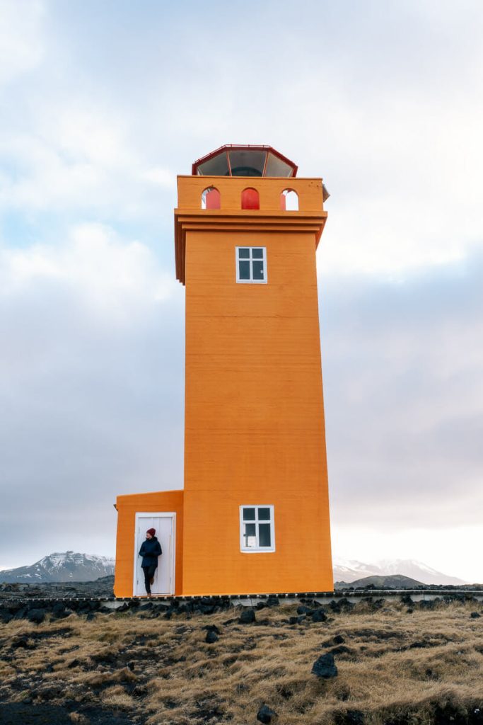 femme posant devant la porte du phare orange de Svörtuloft sur la péninsule de Snaefellsnes