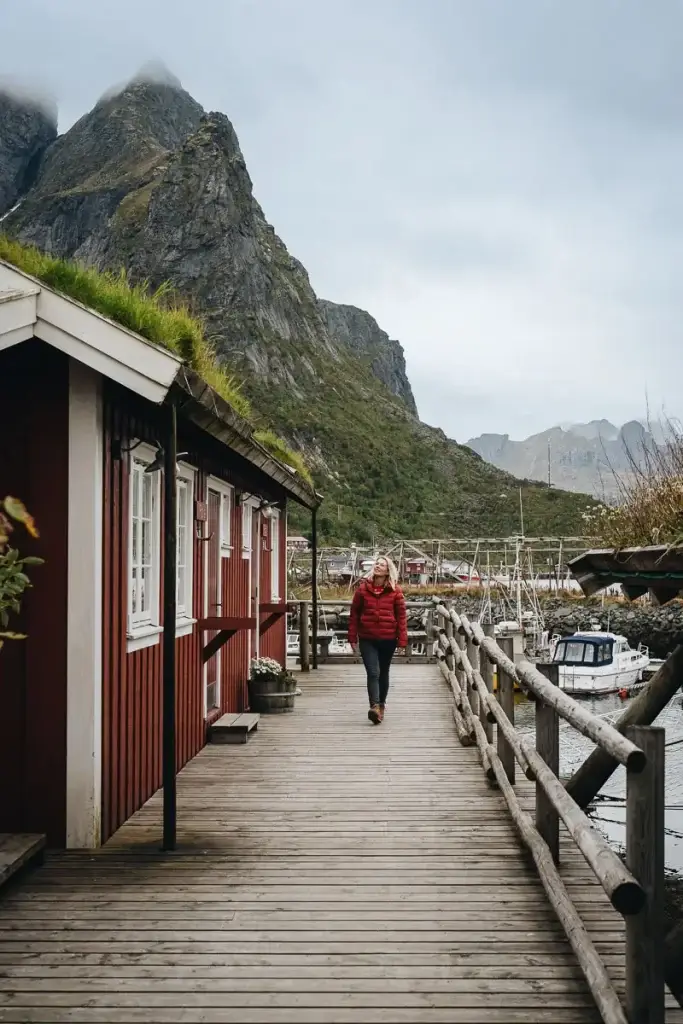 Voyageuse se promenant sur un ponton en bois entre les rorbu rouges, au pied des montagnes de Reine aux îles Lofoten