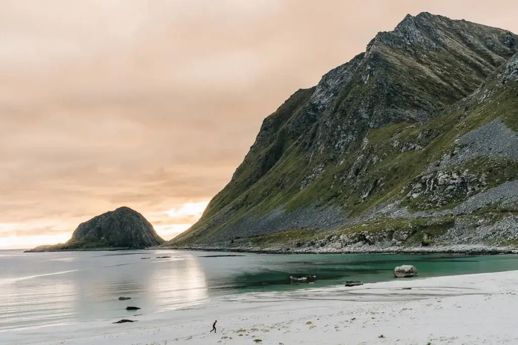 Silhouette courant sur la plage de sable blanc d'Haukland au coucher du soleil, entre eau turquoise et montagnes, aux îles Lofoten