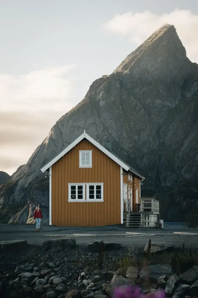 Voyageuse devant une maison de pêcheur jaune de Sakrisøy, au pied du pic d'Olstind aux îles Lofoten