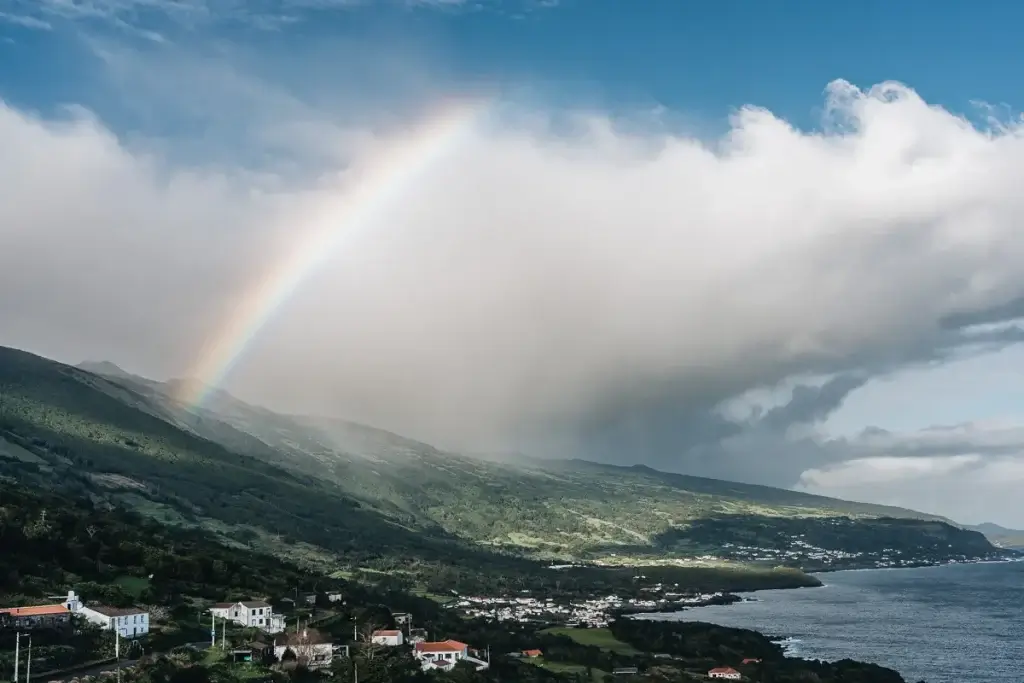 Arc-en-ciel spectaculaire sur le flanc vert du volcan Pico aux Açores, village de São Roque et océan en contrebas