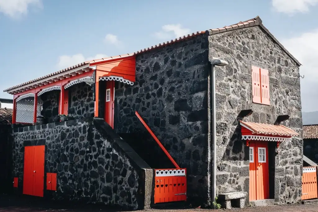 Maison traditionnelle de Lajido sur l'île de Pico aux Açores, pierre de lave noire et boiseries rouges avec motifs de cœurs Légende : L'architecture de Lajido, c'est ce contraste saisissant entre la pierre volcaniq