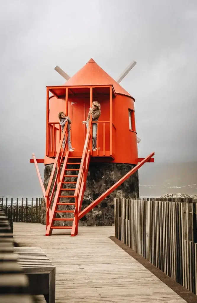 Enfant et adulte explorant un moulin à vent rouge au bord de l'océan à Pico aux Açores
