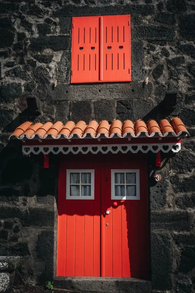 Porte rouge ornée de cœurs découpés sur une maison en pierre de lave noire à Lajido, île de Pico aux Açores