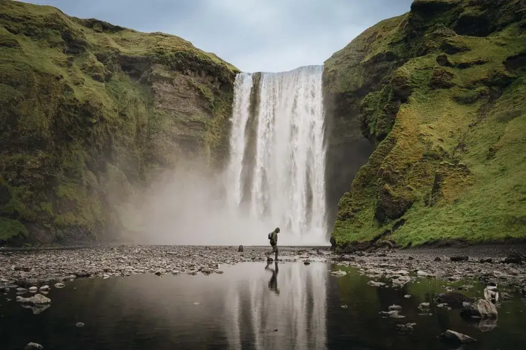 Randonneur marchant face à l'immense cascade de Skógafoss lors d'un road trip en Islande