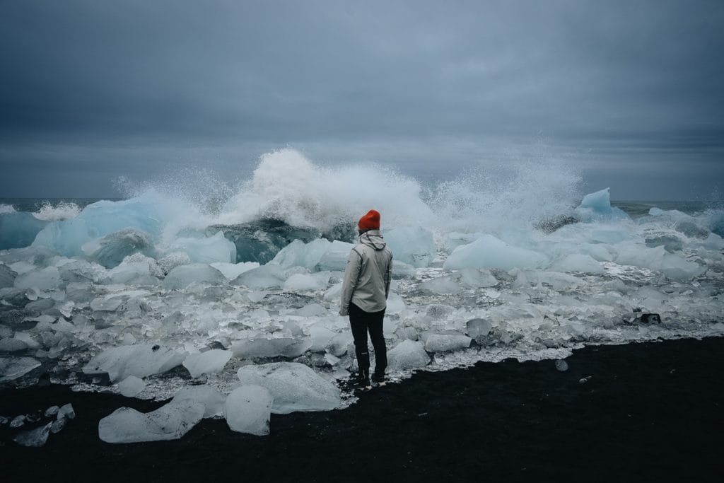 Silhouette d'un voyageur au bonnet orange observant les vagues se fracasser sur les icebergs de Diamond Beach.