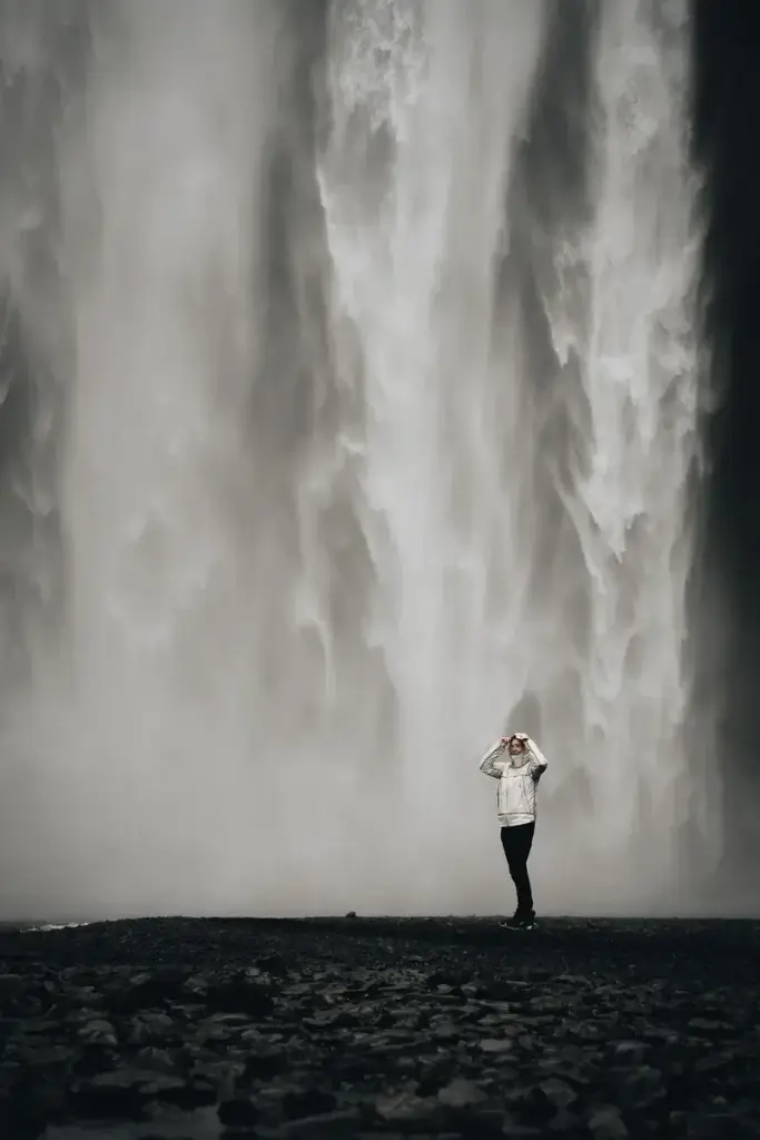 Silhouette d'une voyageuse en veste blanche devant les embruns massifs de la cascade de Skógafoss