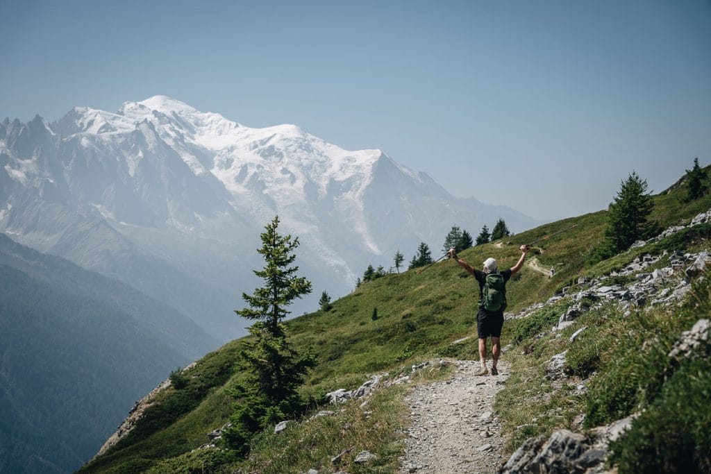 Randonneur levant les bras au ciel sur le sentier en balcon face au massif du Mont-Blanc